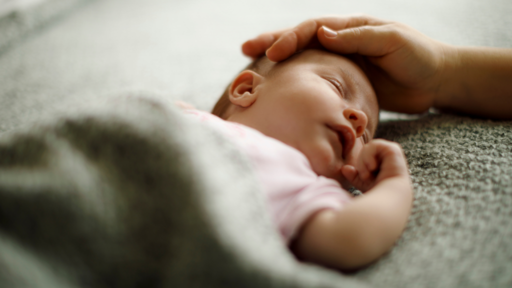 A baby covered in a green blanket, displaying a sign to show how to avoid overheating
